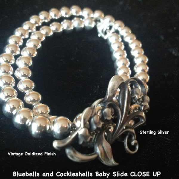 This  pretty and delicate little slide has such detail and femininity. Slip an ecru wired ribbon through this slide and tie it as a choker for a simple, romantic look. Comes with a beautiful ribbon.  Sterling Silver Bluebells and Cockleshells Baby Slide. Part of a beautiful trio of slides which also are beautiful on my Double Wrap Silver Pearls Bracelet.  1-3/8" x 5/8 approximately. Hand made in the USA. Hand Signed.  SILVER PEARLS DOUBLE WRAP BRACELET SOLD SEPARATELY.